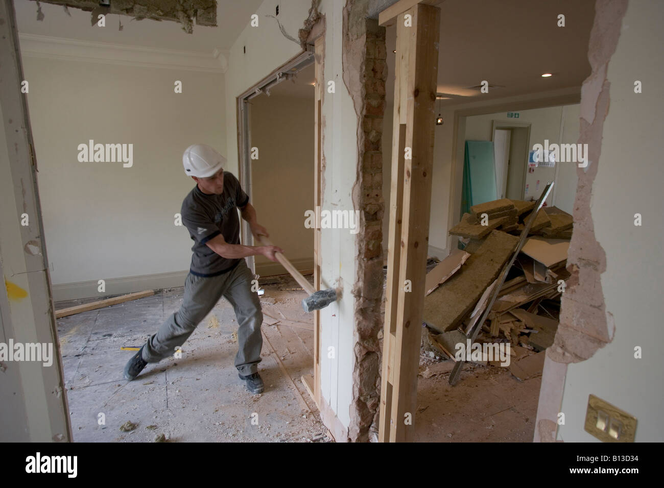 A workman hits a wall with a sledge hammer on a demolition site Stock