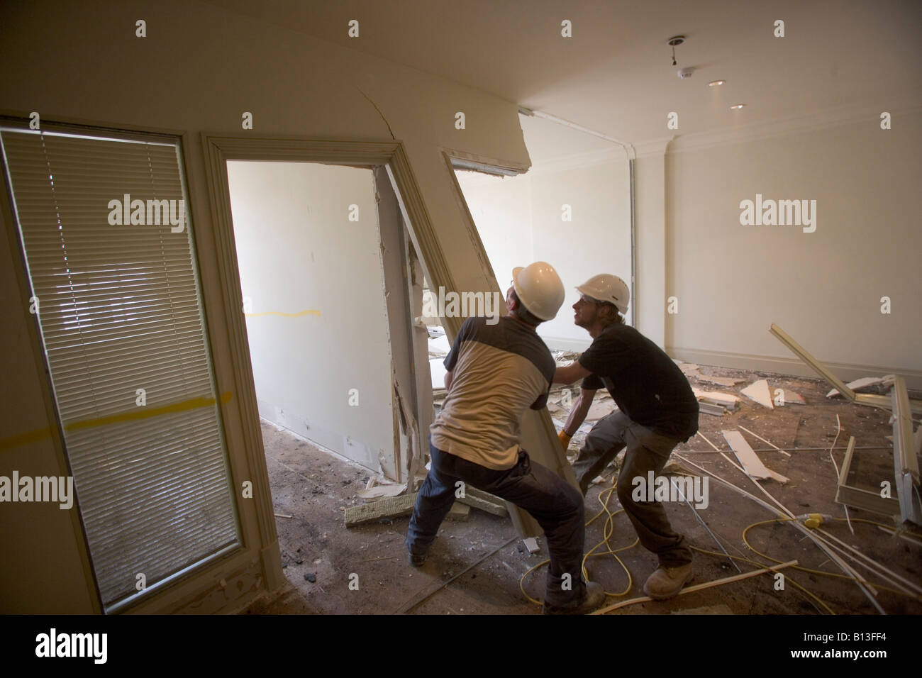 Two workmen pull a wall and doorframe off in a demolition site. Stock Photo