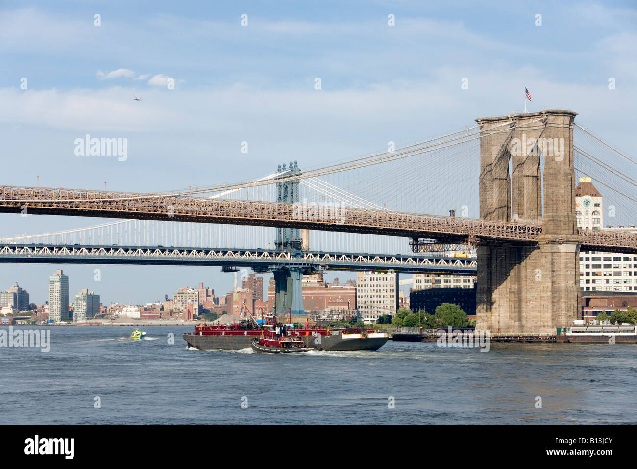 A Tug Boat pushes a cargo ship under New York's Brooklyn Bridge Stock Photo