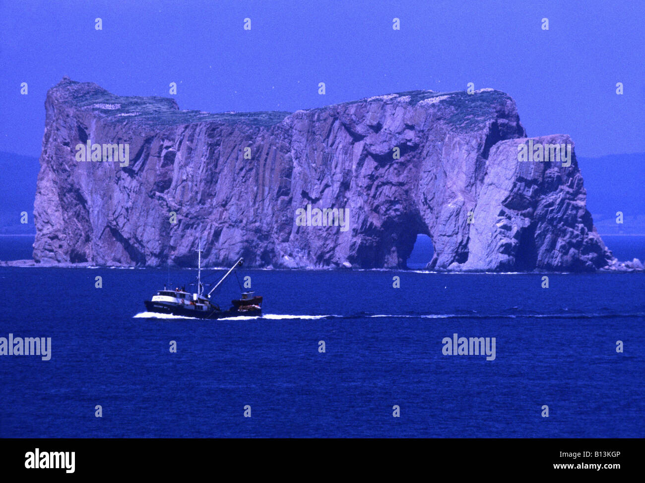 Spectacular Perce rock dwarfs a fishing boat in the Atlantic ocean off Canada's Eastern seaboard