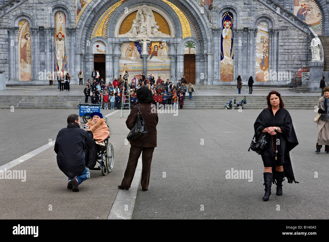 Family, with a child in a wheelchair, outside the church in Lourdes, France Stock Photo