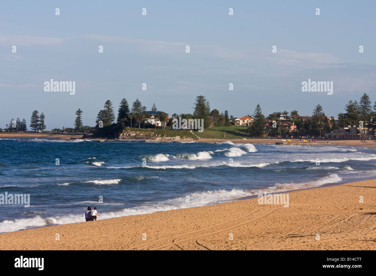 Two people walking along a NSW beach with breakers in the background. Stock Photo