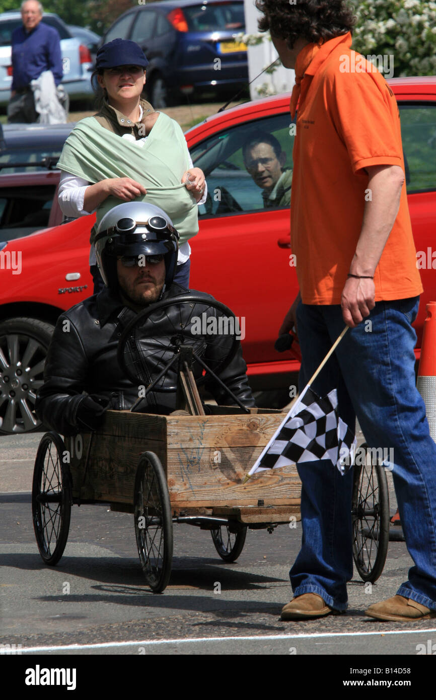 A soapbox downhill racer waits at the start while a man in a red car looks on very interested. Stock Photo