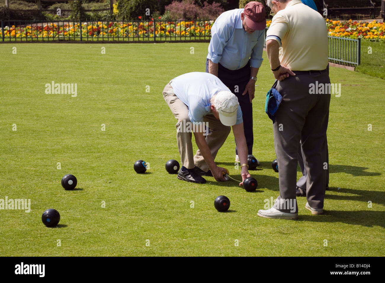 Four seniors retired elderly pensioners gentlemen retirees playing bowls on crown bowling green in public park England UK Britain Stock Photo