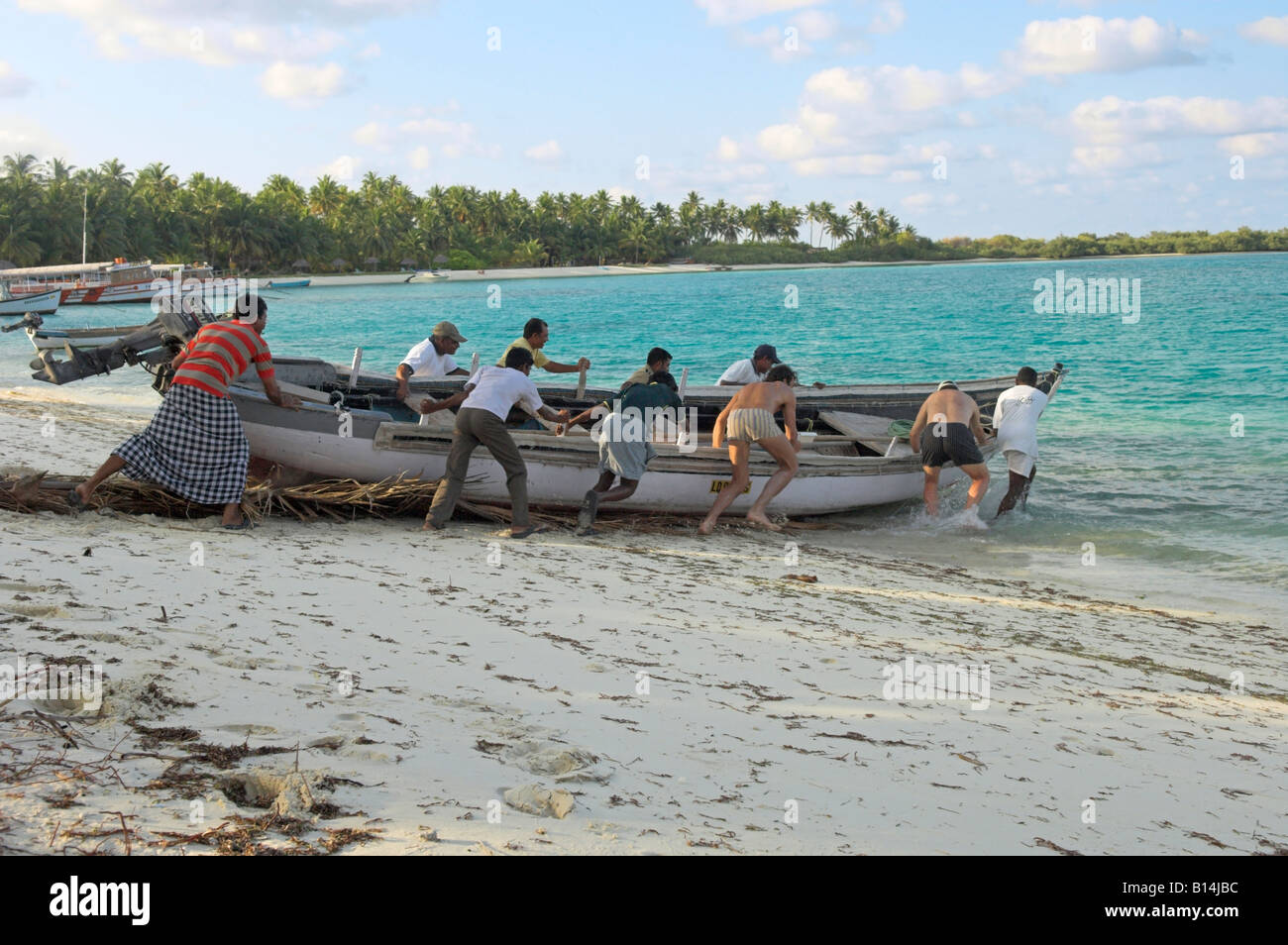 Men launching fishing boat into lagoon from sandy beach Bangaram Island Lakshadweep India Stock Photo
