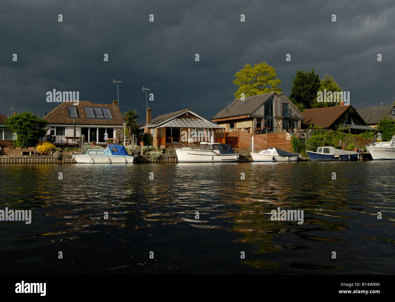 Pleasure boats and riverside houses under black threatening sky, viewed