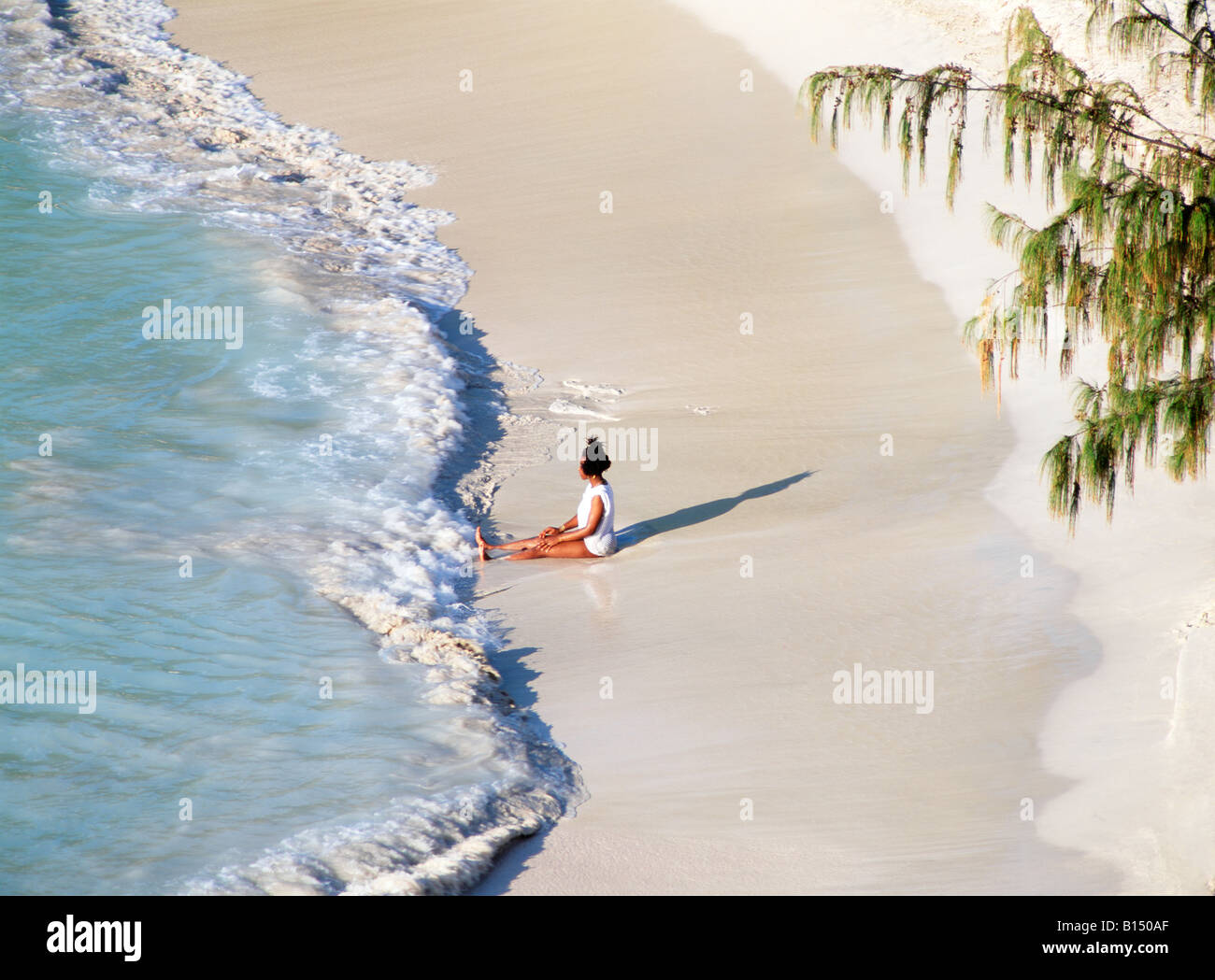 Waves break on white sand beach. Young woman relaxing at Jolly Beach, Coco Beach, west coast of Caribbean island of Antiqua Stock Photo