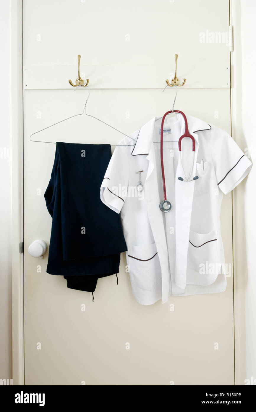 A nurse uniform with stethoscope and fob watch hung up on the back of a door Stock Photo