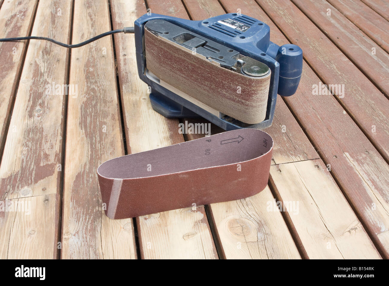 Belt sander on its side showing worn sanding belt on partially sanded wooden decking during