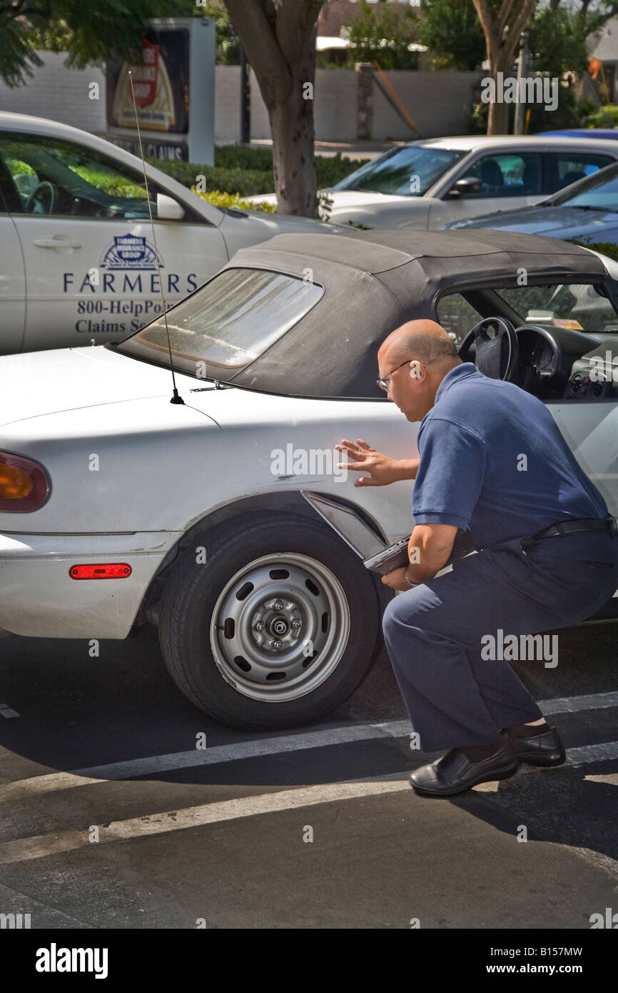 An adjuster evaluates damage to a car for an insurance claim Note laptop and insurance company car in background Stock Photo