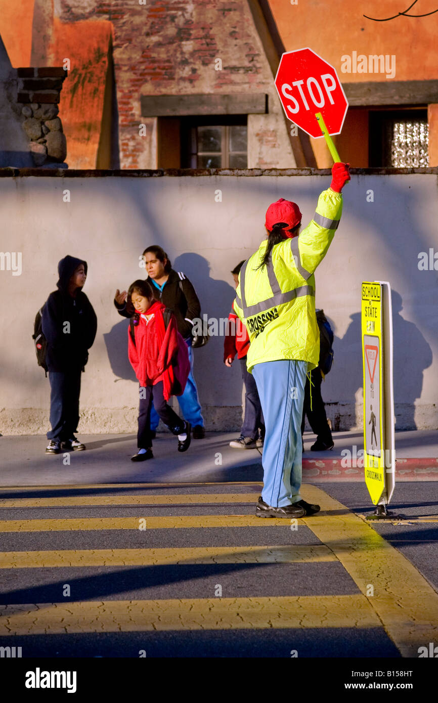 Hispanic school crossing guard controls street traffic as South California elementary school students and parents arrive in AM Stock Photo