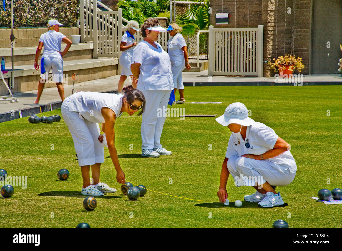 Wearing the regulation white uniforms two woman players measure the distance between two lawn bowling balls at competition Stock Photo