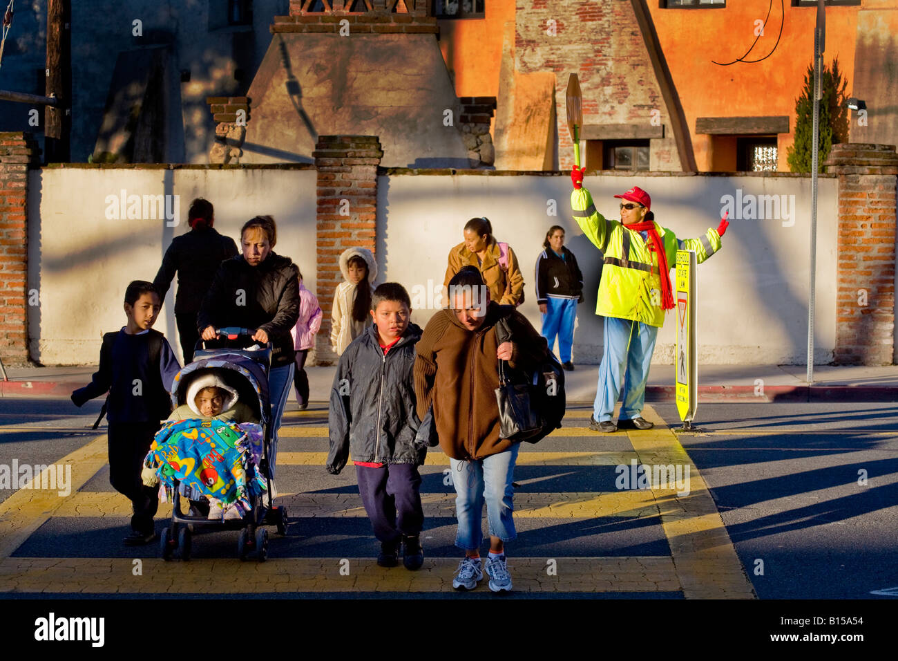Hispanic school crossing guard controls street traffic as South California elementary school students and parents arrive in AM Stock Photo