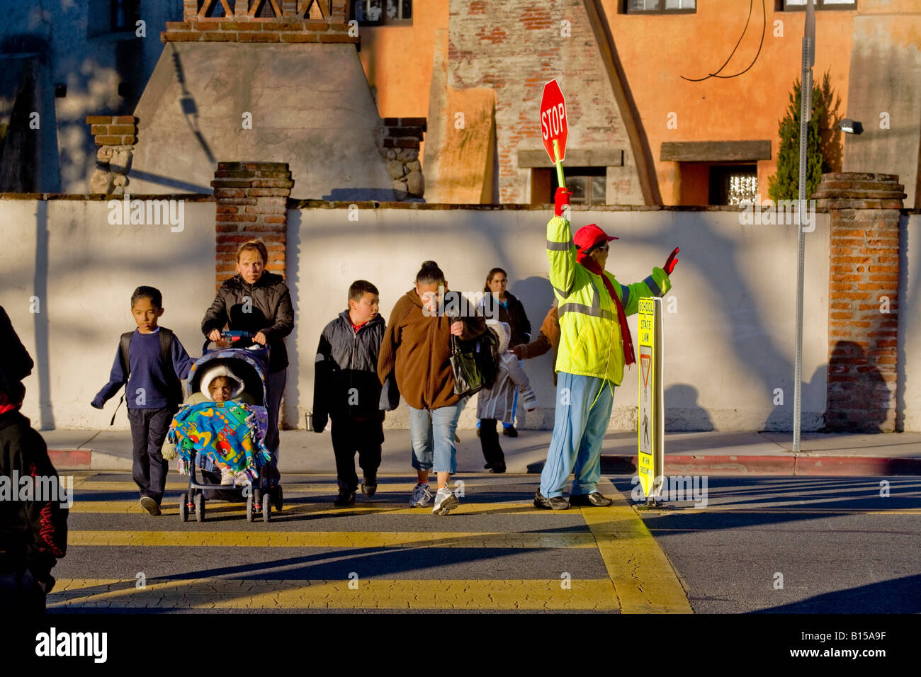 Hispanic school crossing guard controls street traffic as South California elementary school students and parents arrive in AM Stock Photo