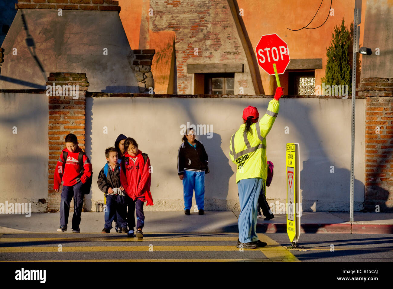 Hispanic school crossing guard controls street traffic as South California elementary school students and parents arrive in AM Stock Photo