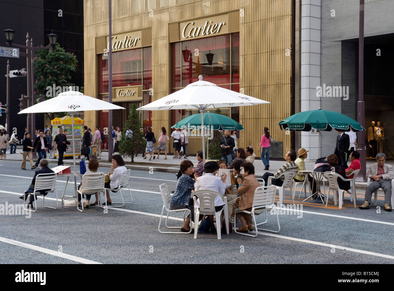 People sitting at tables under parasols on main street in Ginza at weekend when street is pedestrianised in Tokyo 2008 Stock Photo