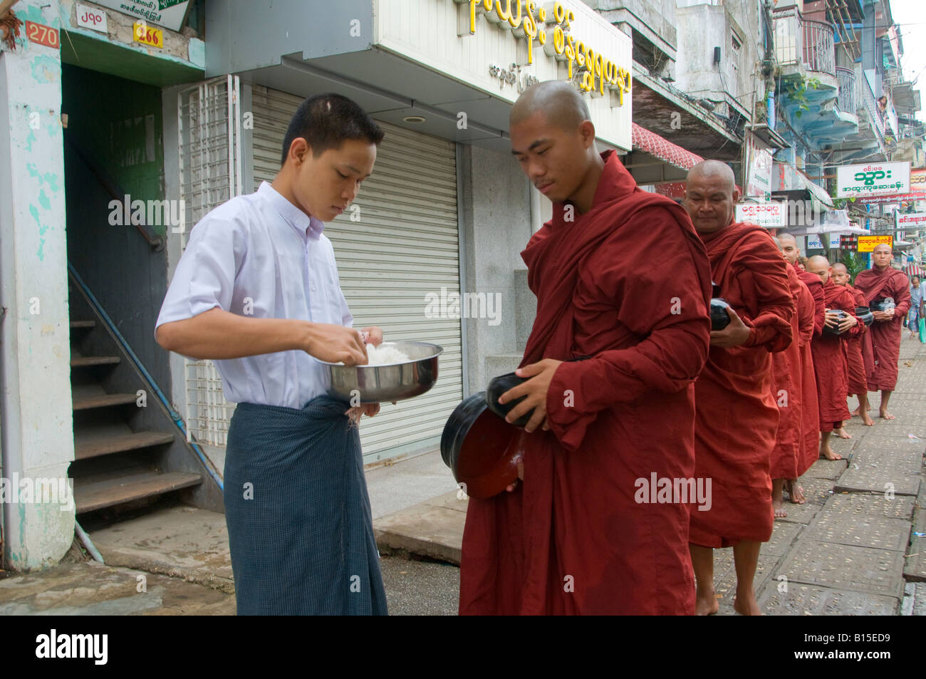 A man serving buddhist monks rice on their morning alms walk in the center of Yangon Myanmar, Burma Stock Photo
