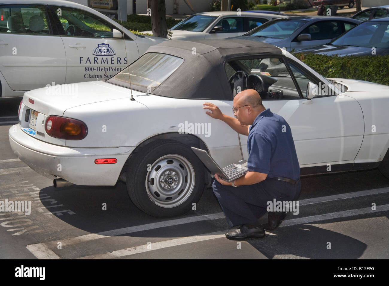 An adjuster evaluates damage to a car for an insurance claim Note laptop and insurance company car in background Stock Photo