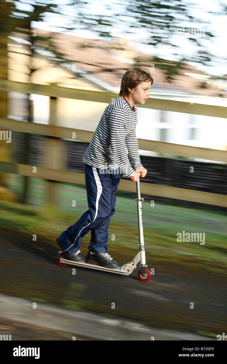 Young boy aged 12 years old riding downhill on a mini scooter in a suburban residential area Stock Photo