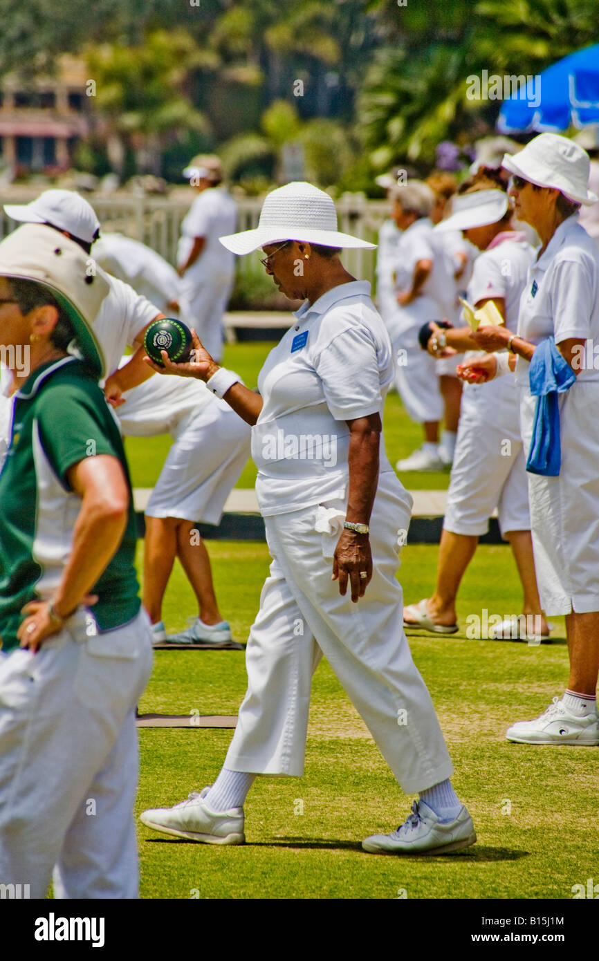 Wearing the regulation white uniform a black woman rolls a bowl ball during a lawn bowling competition in Laguna Beach CA Stock Photo