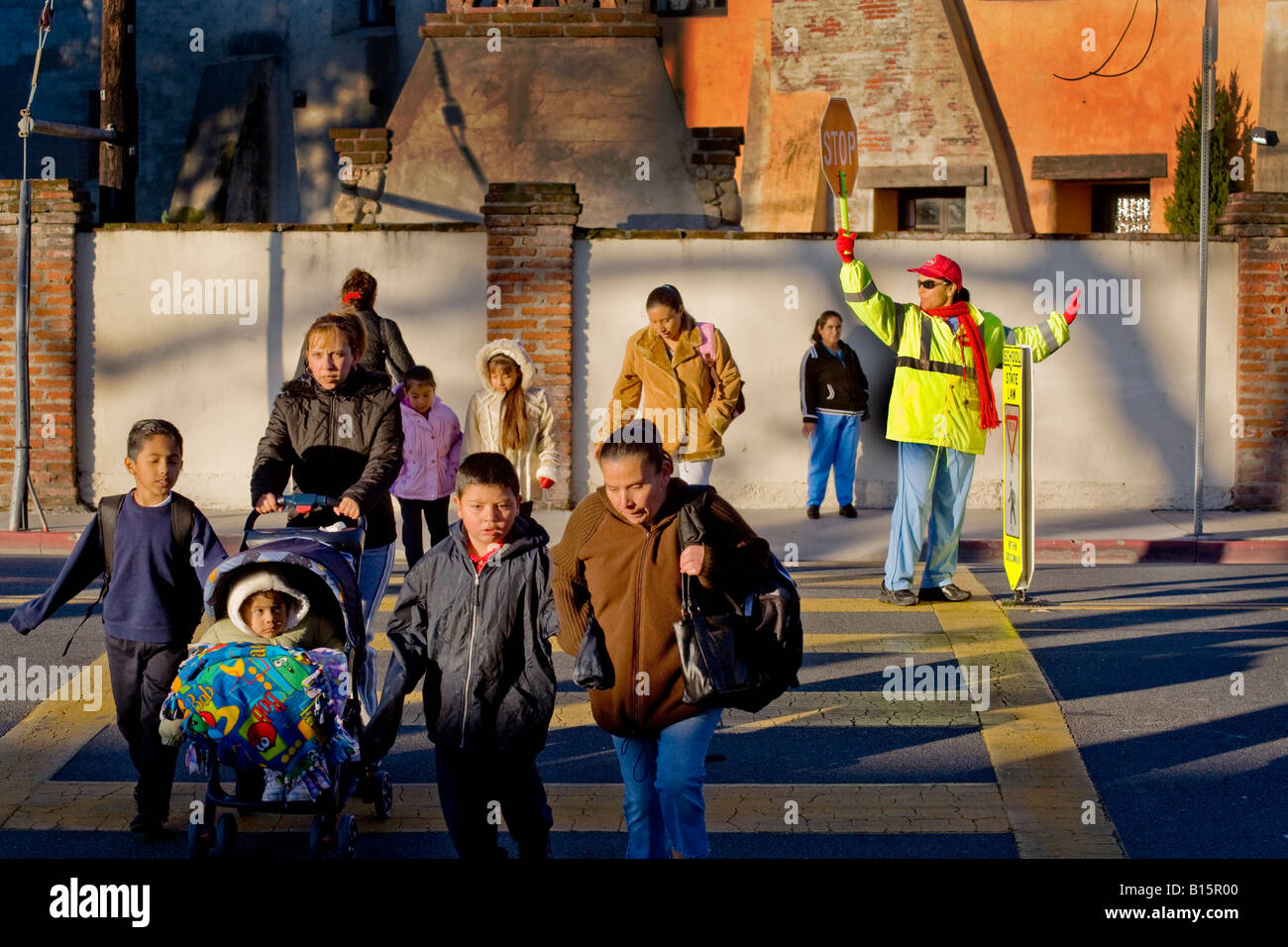 Hispanic school crossing guard controls street traffic as South California elementary school students and parents arrive in AM Stock Photo