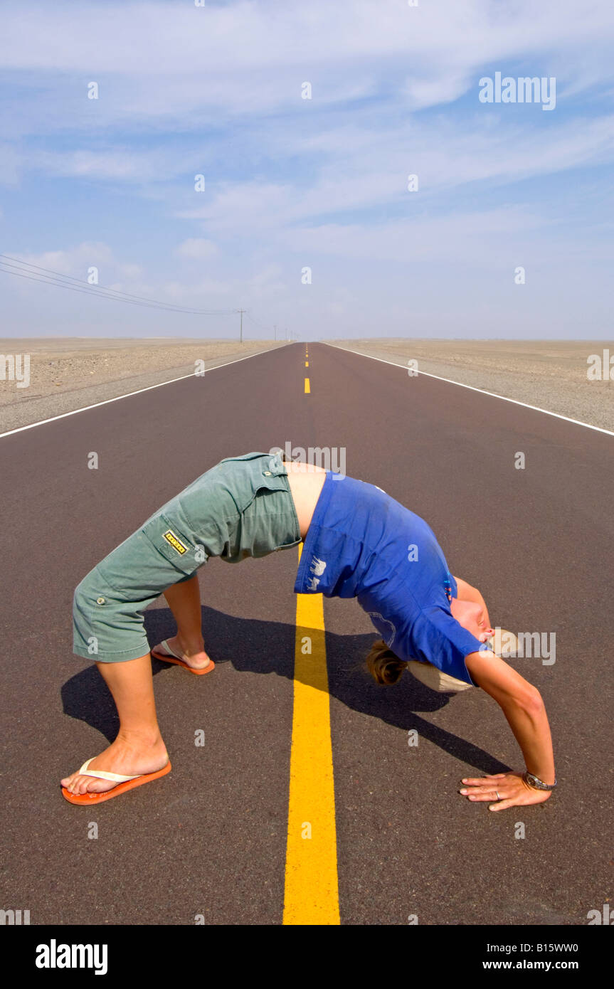 A female in the crab position in the middle of the Pan American Highway leading off to the distance in the desert. Stock Photo
