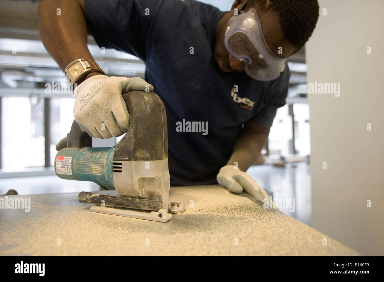 A Workman Cuts A Round Cable Routing Hole In A Desk Stock Photo