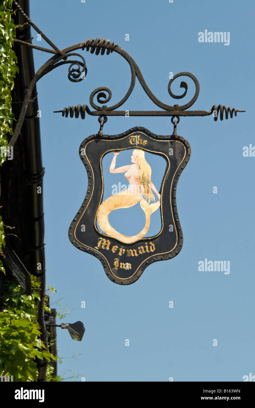 Vertical close up of an old black wrought iron pub sign suspended outside a Tudor building in Rye on a sunny day. Stock Photo