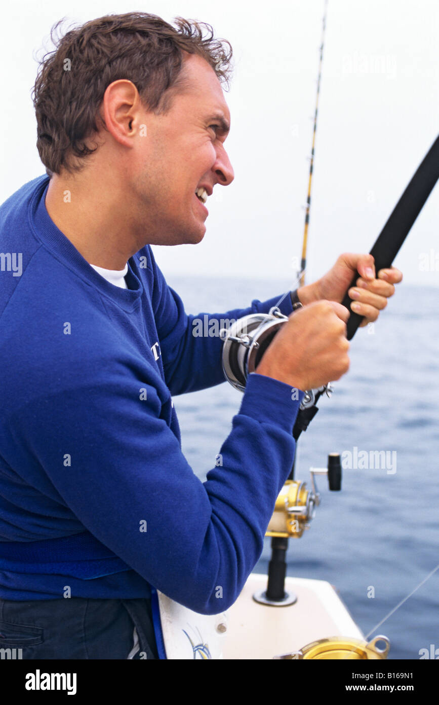 Man with fishing rod, energetically reeling in fish on sport fishing ...