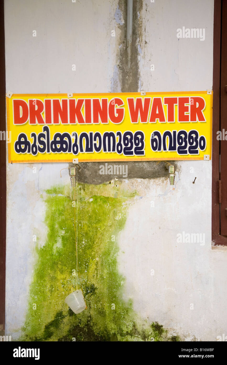 A sign advertises that drinking water is available in both English and Malayam in Palayur, Kerala. A cup hangs from a string. Stock Photo