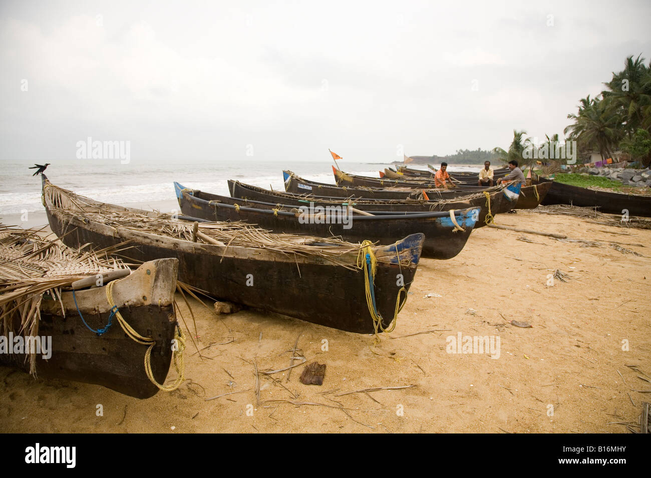 Kappil Beach in Kasaragod, Kerala. Fishing boats are pulled up on the beach. Fishermen sit at their boats. Stock Photo