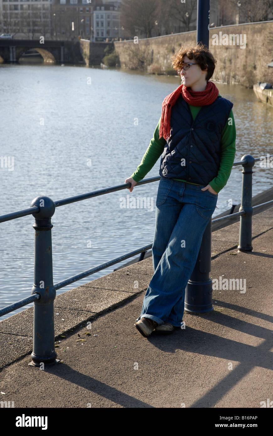 Woman leaning against street lantern post at a riverside looking over the water Stock Photo