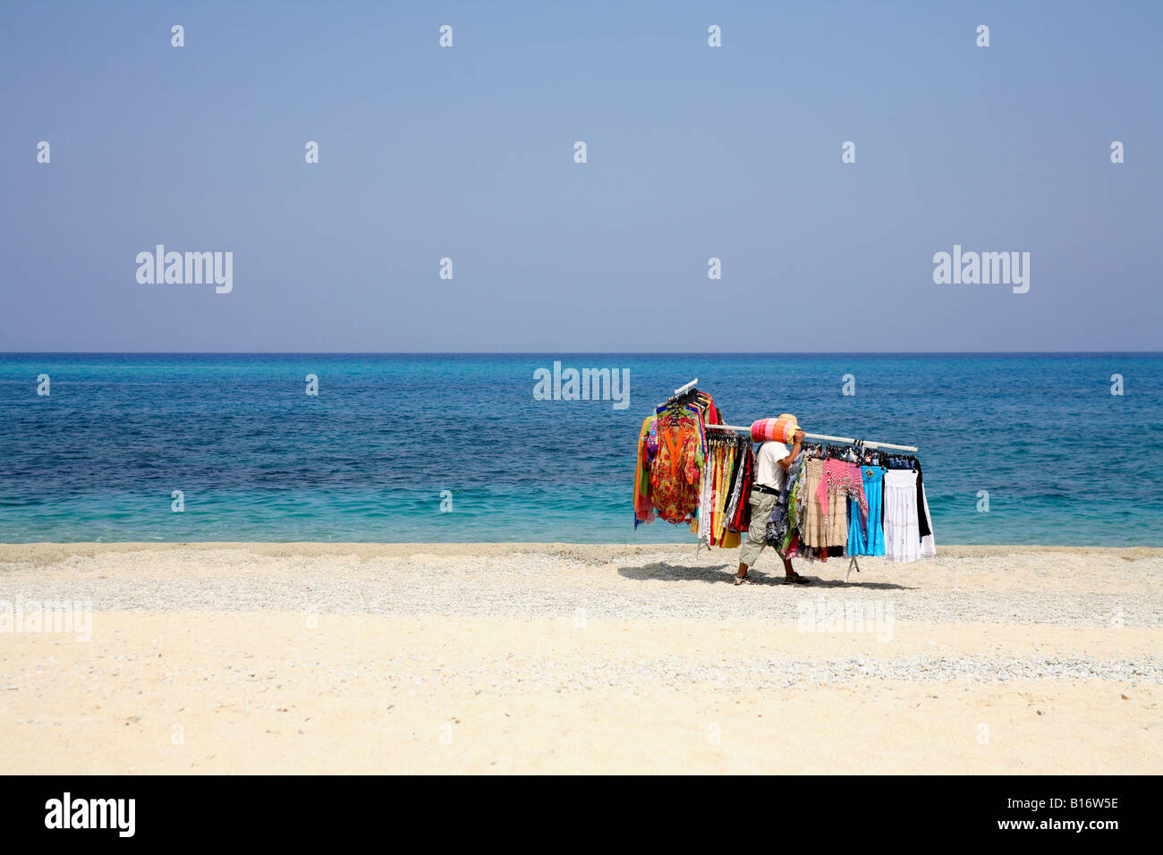 a beach seller walks along the sand carrying a large load of goods to sell to torists and holiday makers. Stock Photo