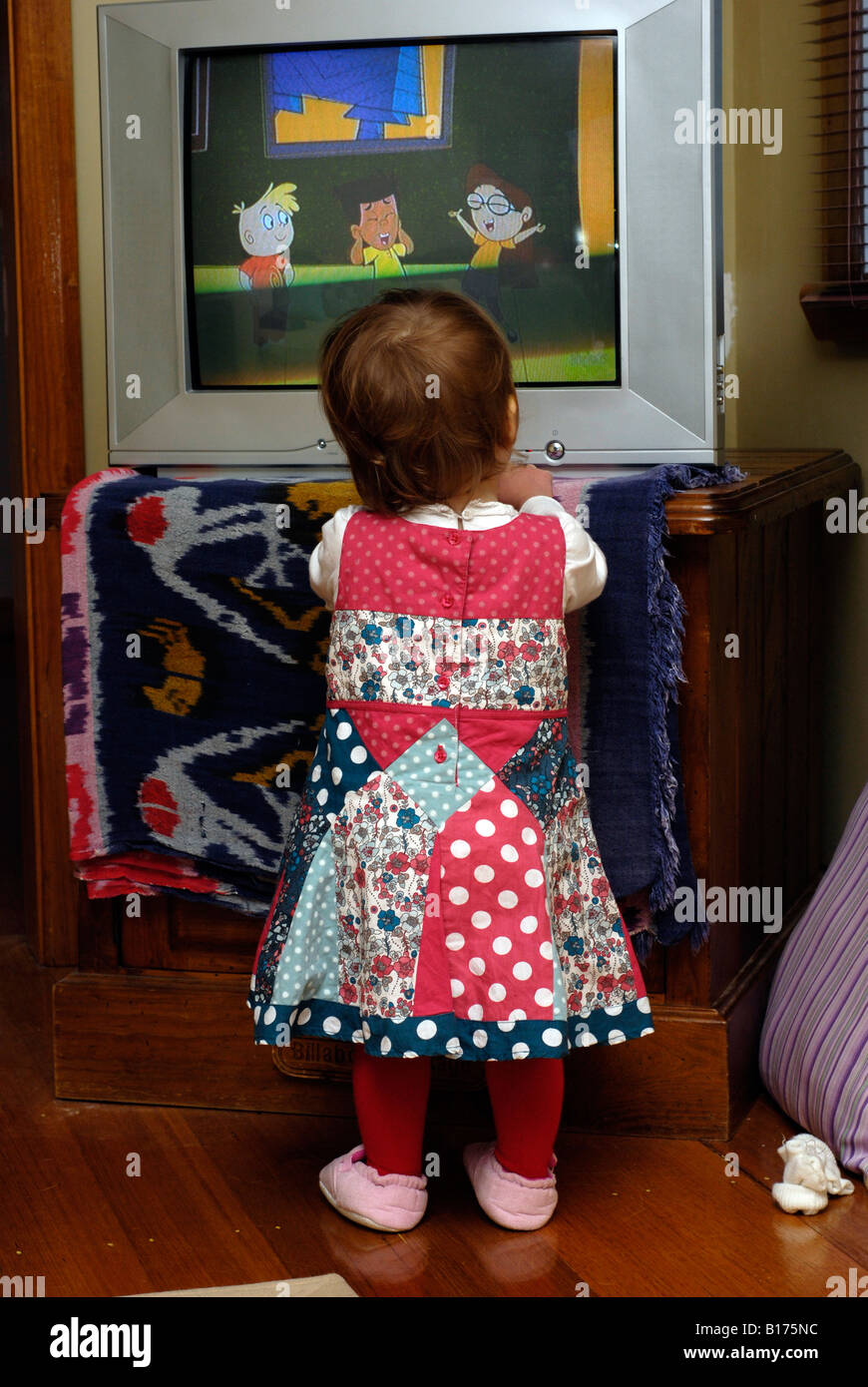 An 18 month old girl standing in front of a television watching children s cartoons Stock Photo