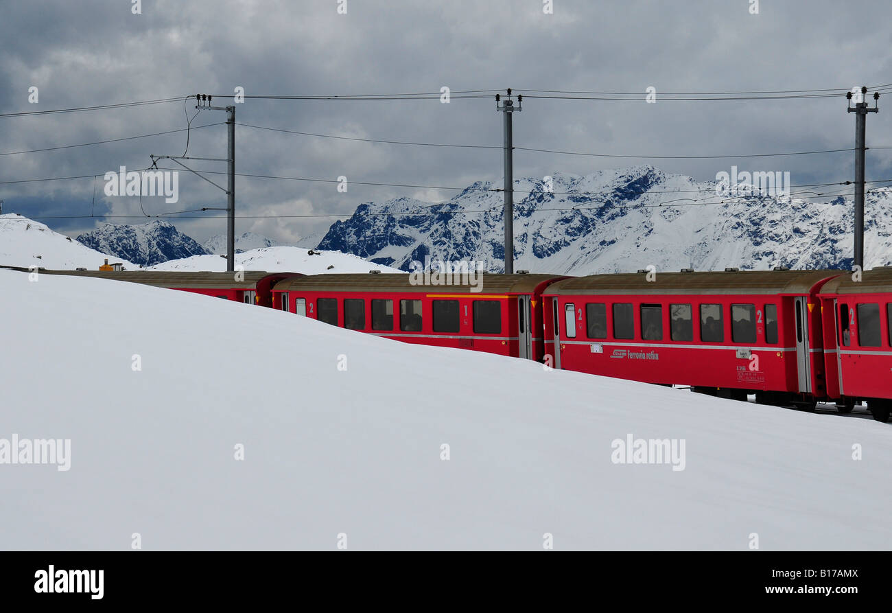 Bright red train carriages appearing from snow covered mountain slopes in the Swiss alps. Full of tourists on a sking holiday. Stock Photo