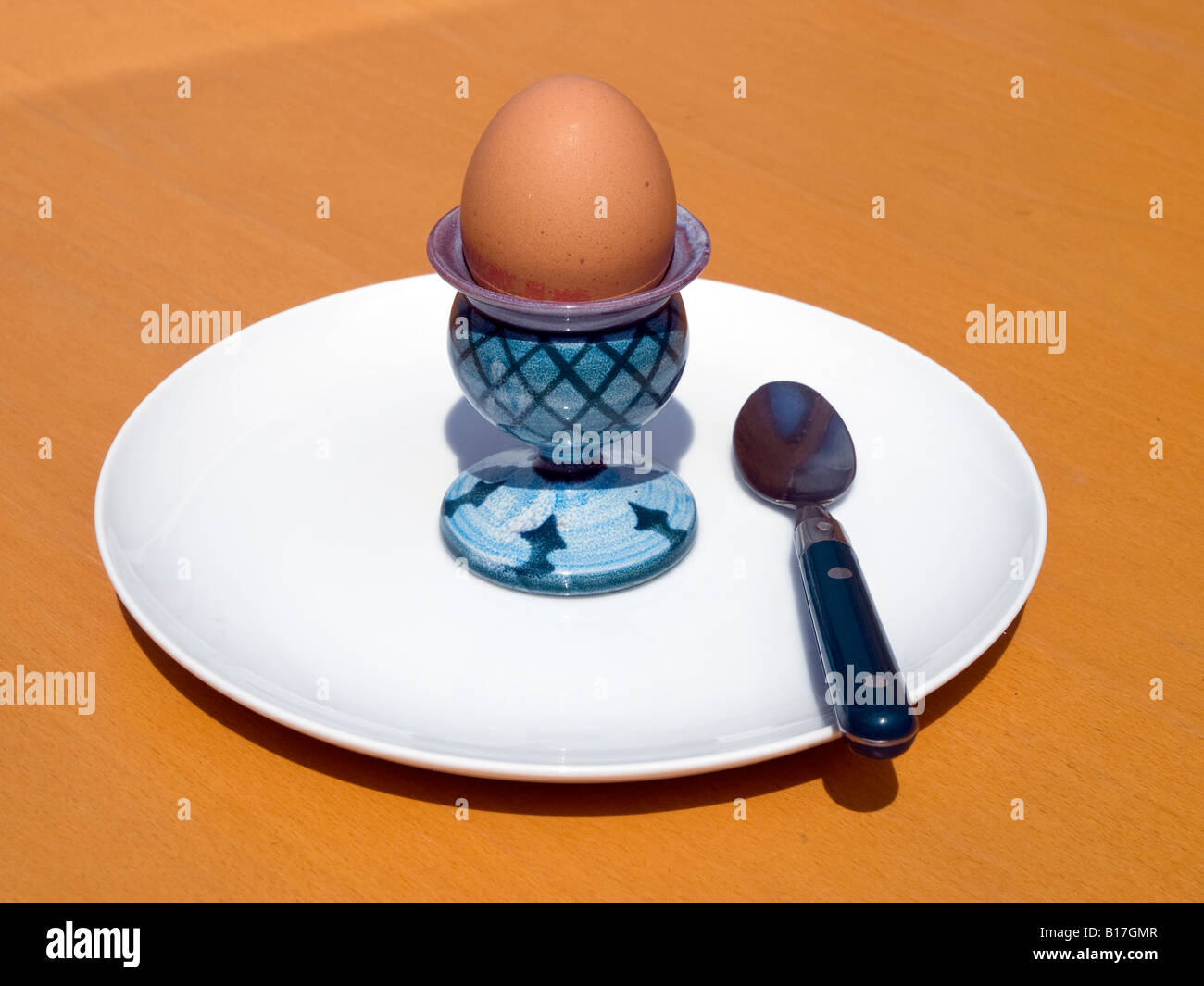 boiled egg in eggcup with teaspoon on white plate set on sunlight light brown table. Stock Photo