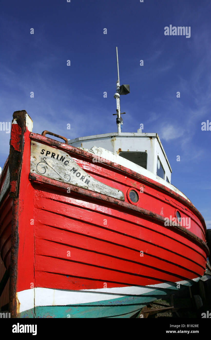 Red and white wooden boat in dry dock against a blue sky Stock Photo