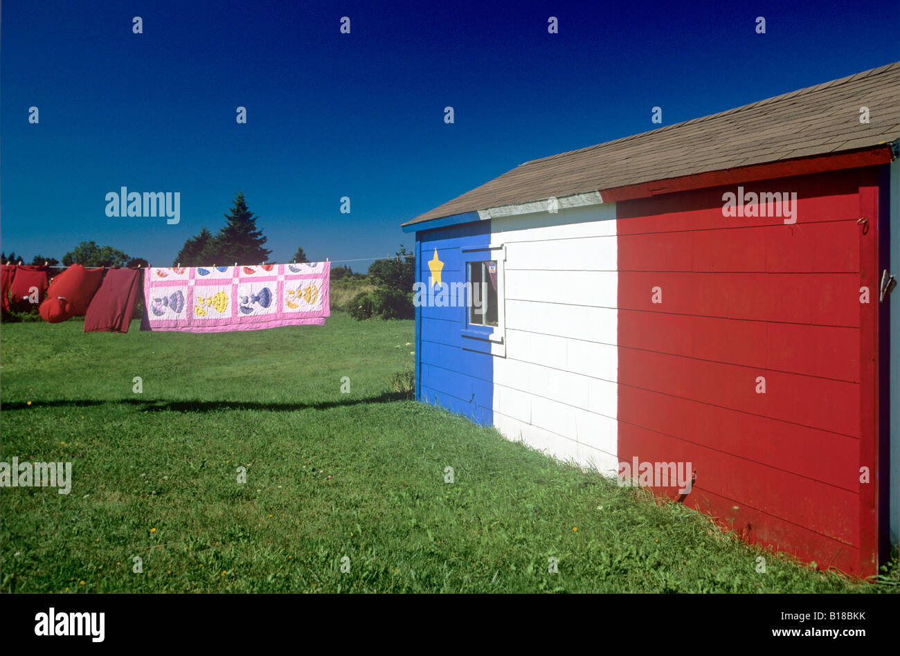 Quilt hanging on clothes line and Acadian flag painted barn, St. Bernard, Nova Scotia, Canada