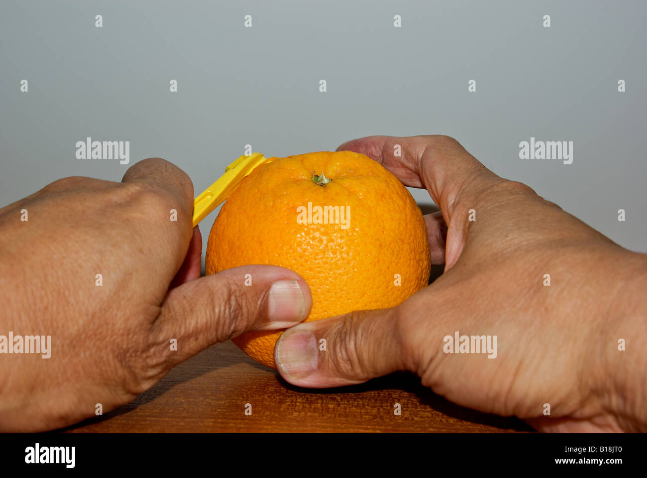 Peeling a navel orange first scoring the cap rind with a peeling tool Stock Photo