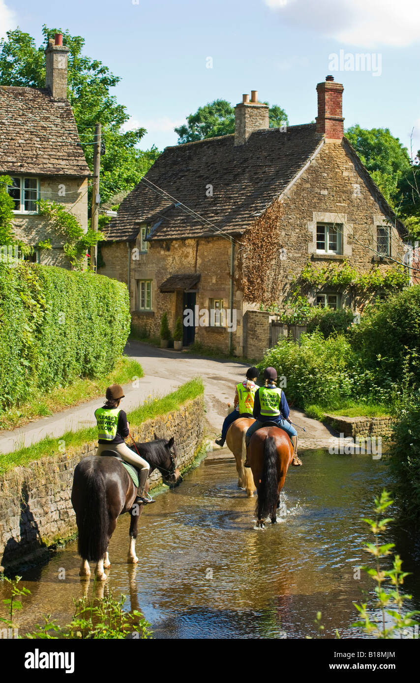 Young female horse riders progressing through ford over the Bybrook stream in Lacock Stock Photo