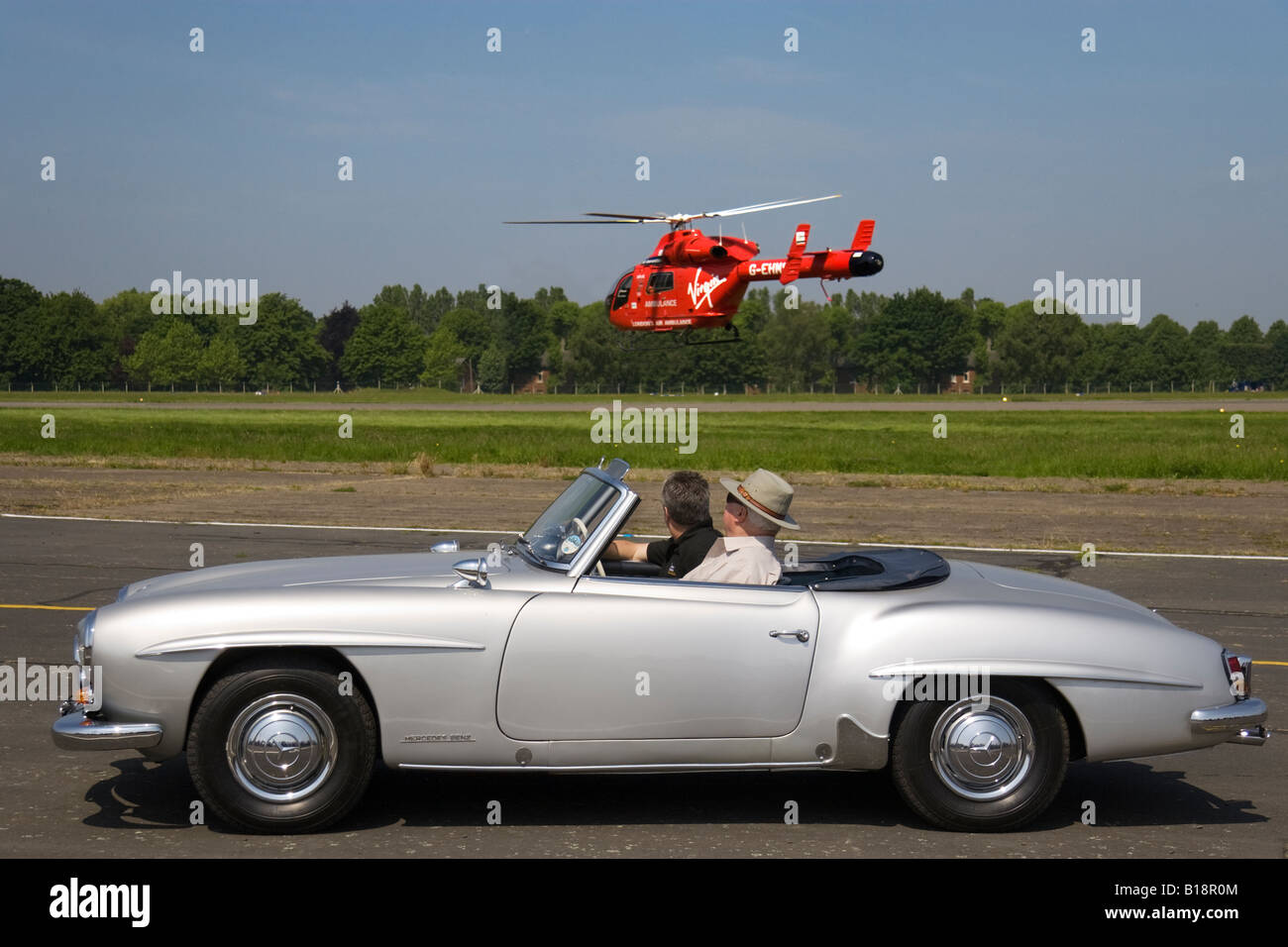 A vintage Mercedes Benz 190 SL Roadster with the Virgin sponsored London Air Ambulance helicopter hovering in the background Stock Photo