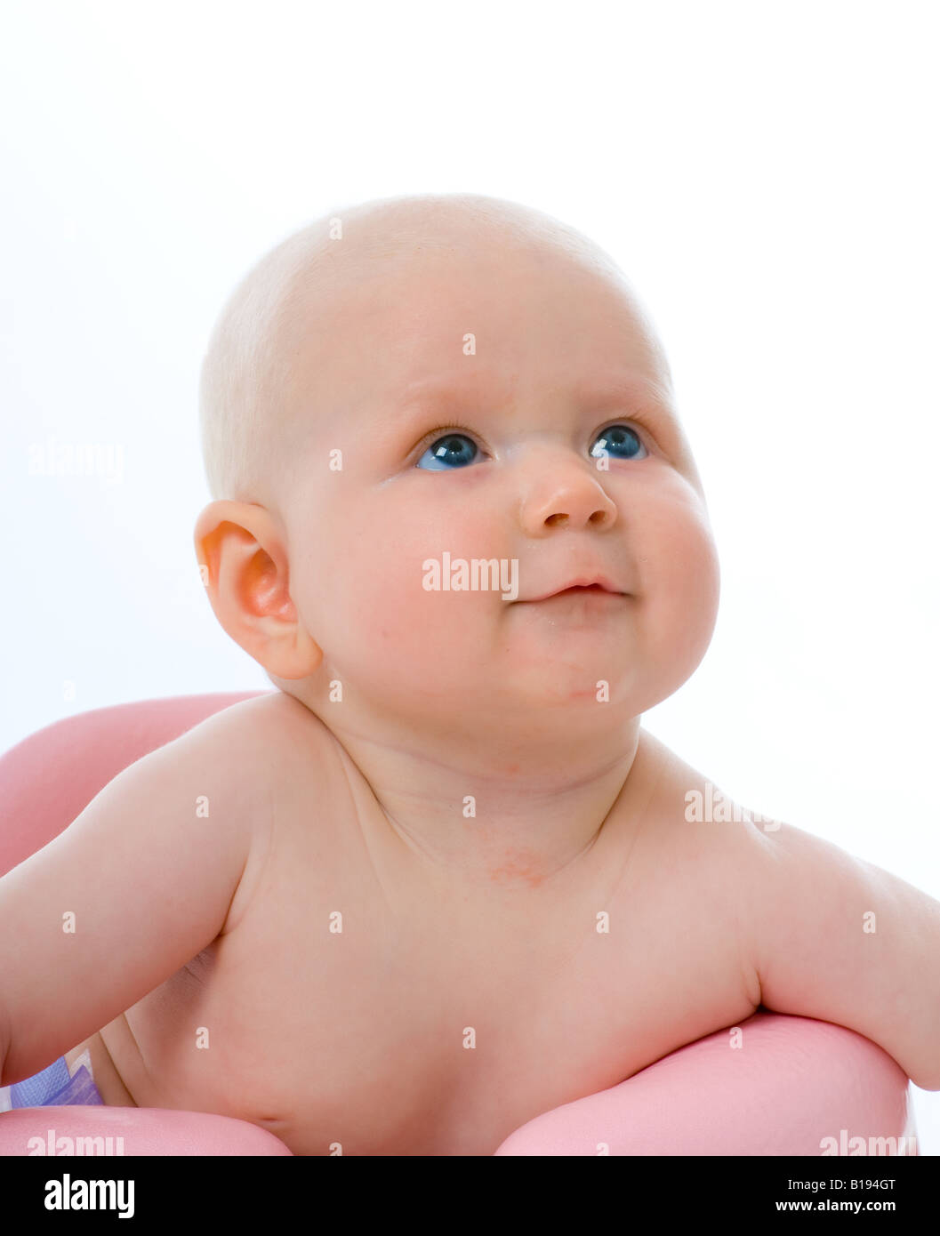 Head and shoulders shot of a young baby sittingup aided by a pink cushioned support Stock Photo