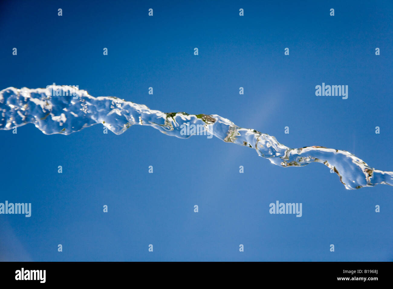 Jet of water frozen against a bright blue sky. Stock Photo