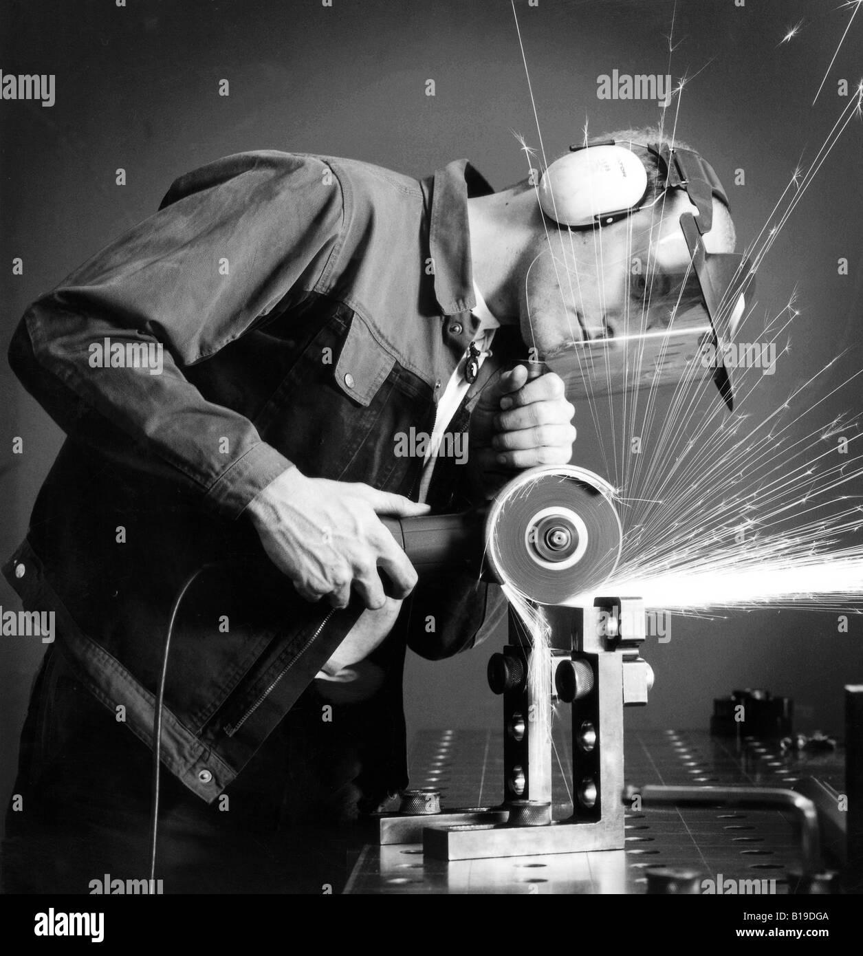 metalworker with hand grinder and safety mask grinding a piece of metal