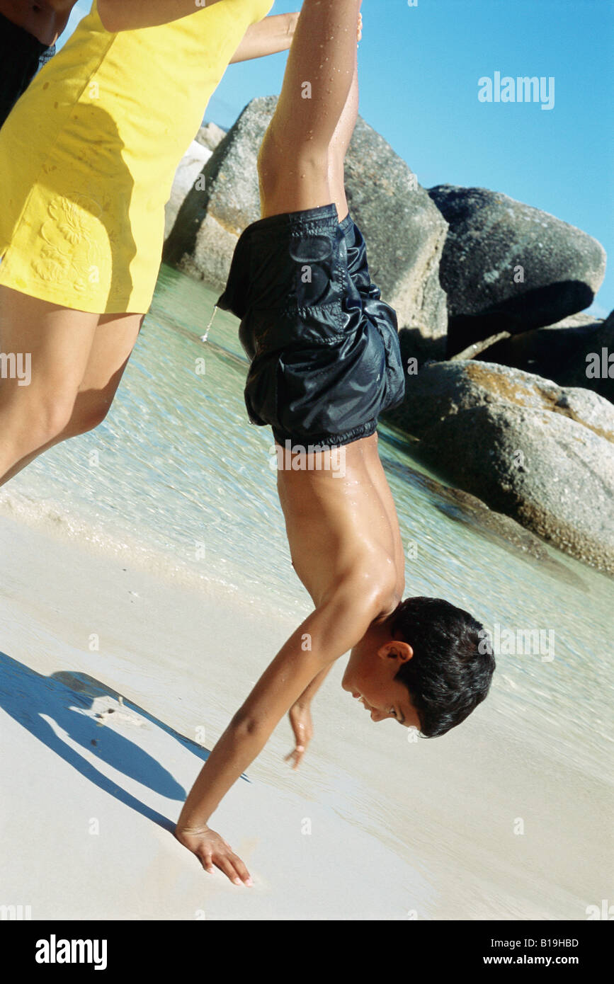 Woman helping boy do handstand on beach Stock Photo