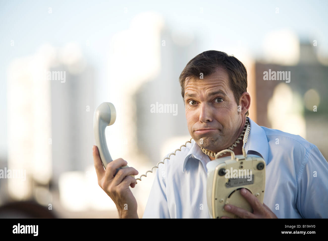 Man holding landline phone, cord wrapped around his neck, looking at camera Stock Photo