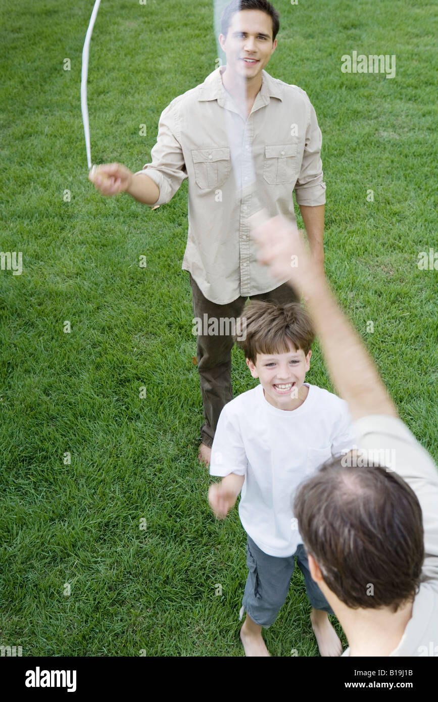 Boy playing jump rope with two men, smiling, cropped view Stock Photo ...