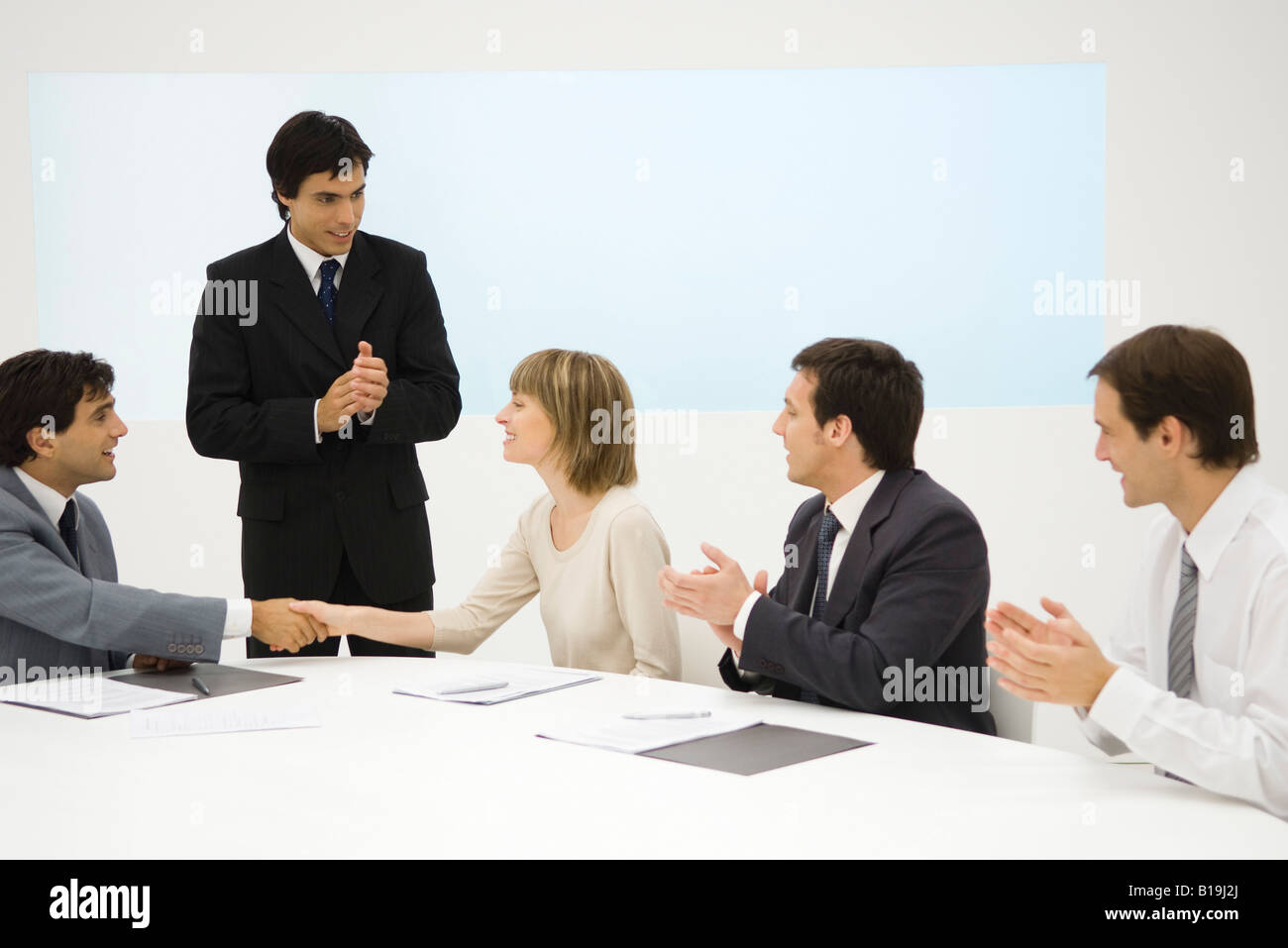 Business associates at conference table, two shaking hands, the others clapping Stock Photo