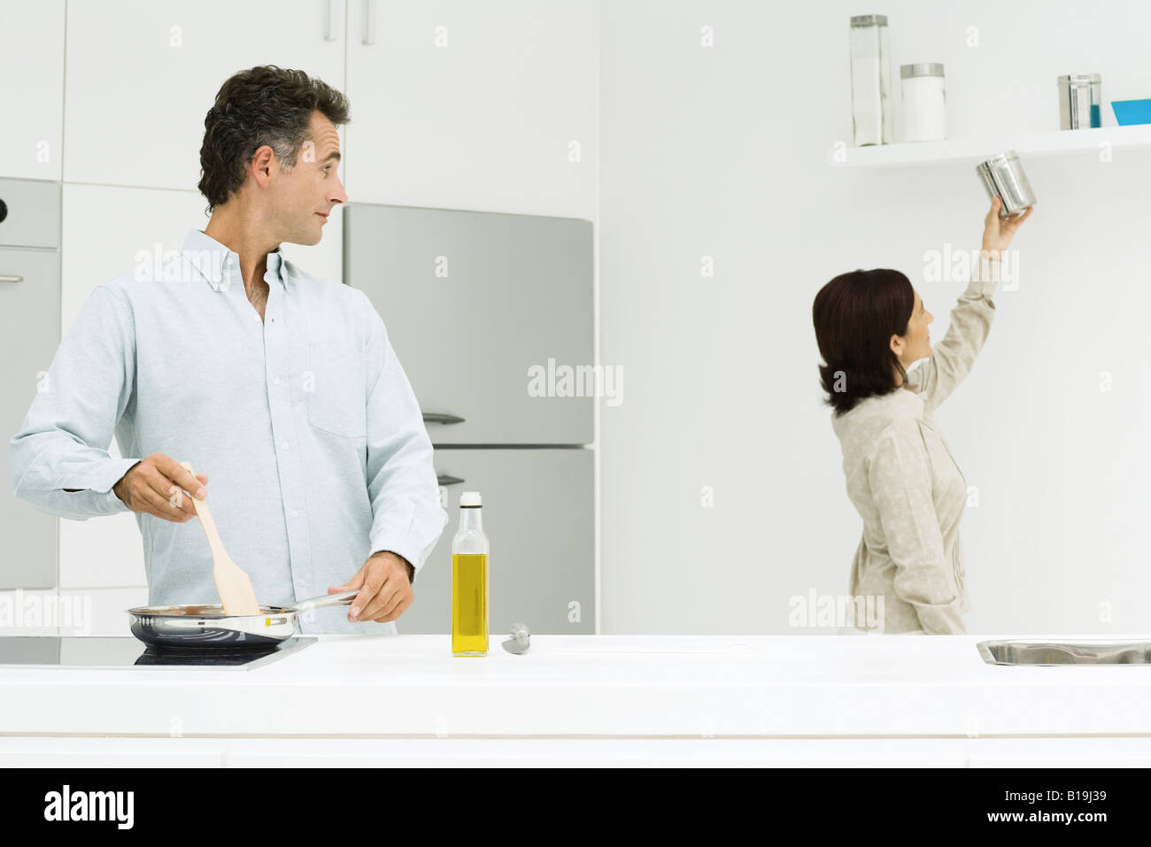 Couple in kitchen, man cooking at stove, looking over shoulder, wife