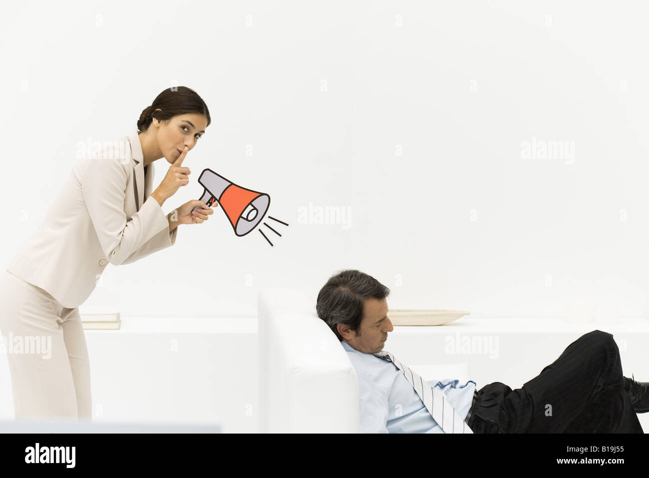 Man sleeping in chair, woman behind him holding megaphone, looking at camera, finger over lips Stock Photo